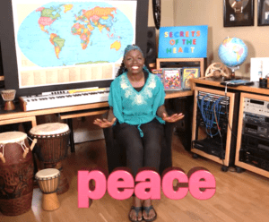 Black woman from Secrets of the Heart TV video signing the word peace in American Sign Language. The word peace is written on the screen in large pink letters.