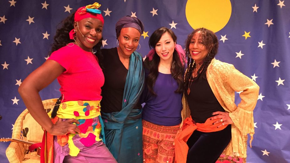 Four female artists of various ethnicities wearing colorful clothing and standing in front of a backdrop of a starry night.